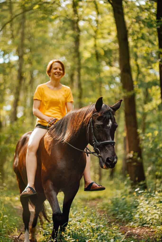 Jezdkyně v lese na hnědákovi, oděná do žlutého trička a kraťasů.